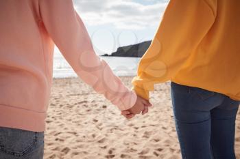 Close Up Of Mother And Daughter Holding Hands On Winter Beach Vacation
