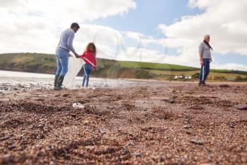 Multi-Generation Family Collecting Litter On Winter Beach Clean Up With Focus On Foreground