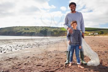 Portrait Of Father And Son Collecting Litter On Winter Beach Clean Up