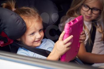 Two Young Girls Watching Digital Tablet In Back Seat On Car Journey