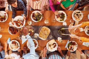 Overhead Shot Of Multi-Generation Family Sitting Around Table Enjoying Meal At Home Together