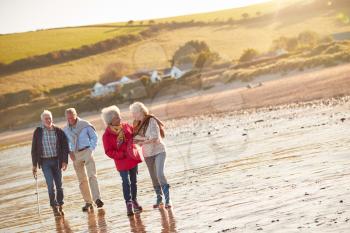 Group Of Smiling Senior Friends Walking Arm In Arm Along Shoreline Of Winter Beach