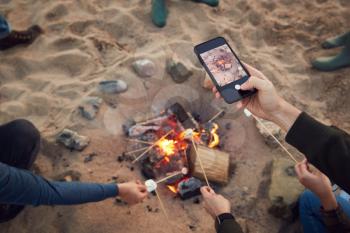 Close Up Of Taking Photo Of Toasting Marshmallows Around Fire On Beach With Mobile Phone