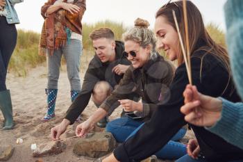 Group Of Young Friends Toasting Marshmallows Around Fire On  Beach Vacation