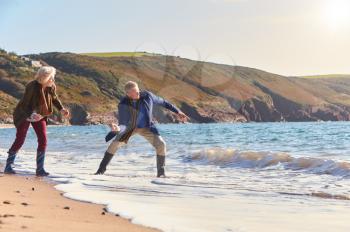 Senior Couple Skimming Stones Across Waves As They Walk Along Beach Together
