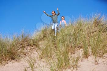 Two Girls Having Fun On Beach Vacation Running Down Sand Dunes