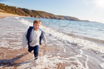Young Boy Having Fun Running Through Waves On Beach