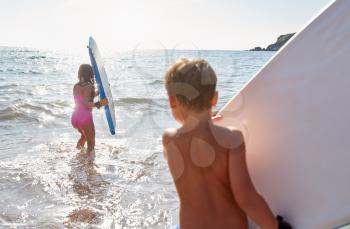 Children Playing In Sea With Bodyboards On Summer Beach Vacation