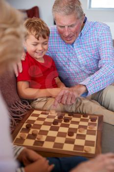 Grandparents Playing Board Game Of Draughts With Grandchildren At Home