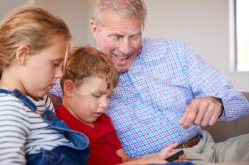 Grandfather Playing Video Games With Grandchildren On Mobile Phones At Home