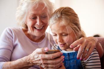 Grandmother Playing Video Game With Granddaughter On Mobile Phone At Home