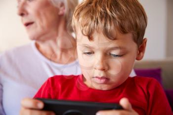 Grandmother Playing Video Game With Grandson On Mobile Phone At Home