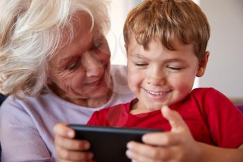 Grandmother Playing Video Game With Grandson On Mobile Phone At Home