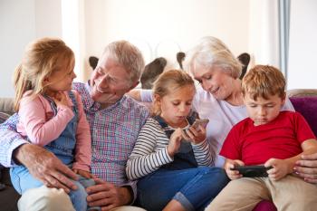 Grandparents Playing Video Games With Grandchildren On Mobile Phones At Home