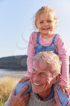 Grandfather Giving Granddaughter Ride On Shoulders As They Walk Through Sand Dunes