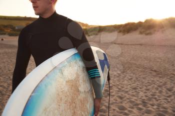 Close Up Of Young Man Wearing Wetsuit Enjoying Surfing Staycation On Beach As Sun Sets