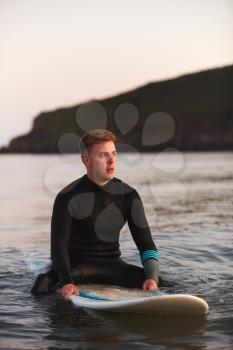 Man Wearing Wetsuit Sitting And Floating On Surfboard On Calm  Sea