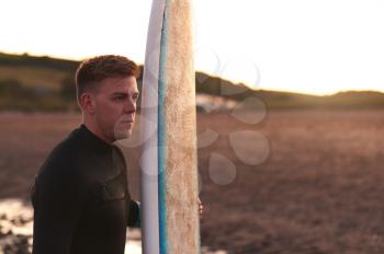 Young Man Wearing Wetsuit Enjoying Surfing Staycation On Beach As Sun Sets