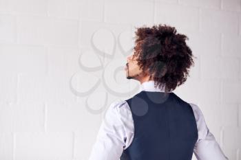 Rear View Of Young Businessman Wearing Suit Standing Against White Studio Wall