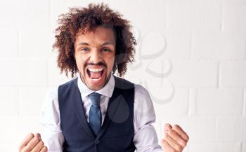 Portrait Of Happy Young Businessman Wearing Suit Celebrating Standing Against White Studio Wall