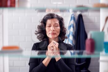 View Through Bathroom Cabinet Of Mature Businesswoman Praying