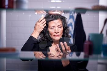 View Through Bathroom Cabinet As Businesswoman Checks Messages On Mobile Phone And Checks Hair