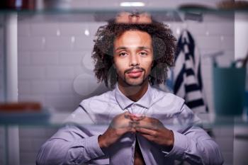 View Through Bathroom Cabinet Of Young Businessman Putting On Shirt Getting Ready For Work