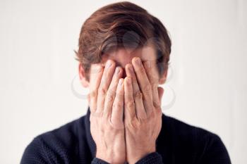 Studio Shot Of Unhappy Man Covering Face With Hands