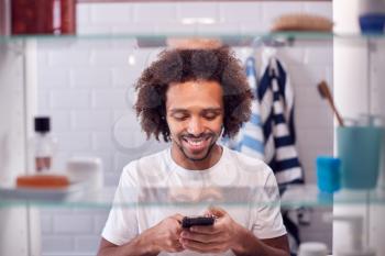 View Through Bathroom Cabinet Of Man Checking Messages On Phone Before Going To Work