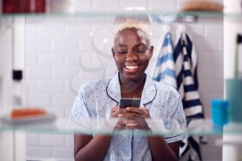 View Through Bathroom Cabinet Of Woman Checking Messages On Phone Before Going To Work