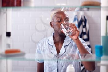 View Through Bathroom Cabinet Of Woman Drinking Glass Of Water