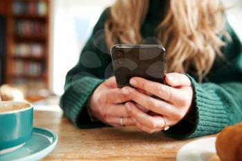 Close Up Of Woman Using Mobile Phone Sitting At Table  In Cafe