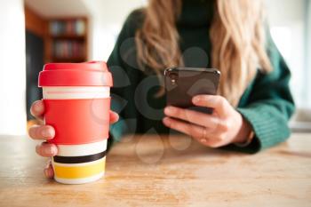 Close Up Of Woman Using Mobile Phone With Reusable Takeaway Drink Cup Sitting At Table  In Cafe