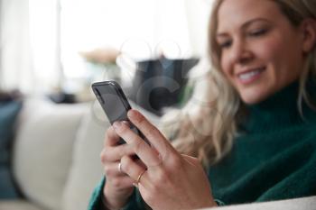 Close Up Of Woman Relaxing On Sofa At Home Using Mobile Phone
