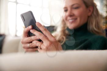 Close Up Of Woman Relaxing On Sofa At Home Using Mobile Phone