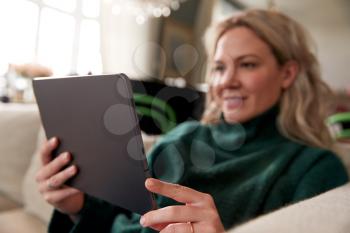 Close Up Of Woman Relaxing On Sofa At Home Using Digital Tablet