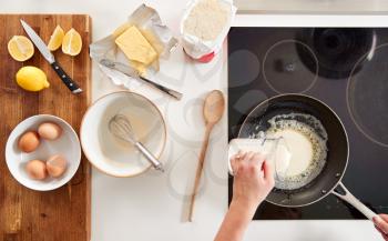 Overhead Shot Of Woman In Kitchen Pouring Batter Into Pan For Pancakes Or Crepes For Pancake Day