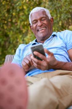 Smiling Senior African American Man Using Mobile Phone Sitting Outdoors In Garden At Home