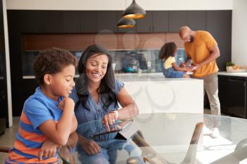 African American Parents Helping Children Studying Homework On Digital Tablets In Kitchen