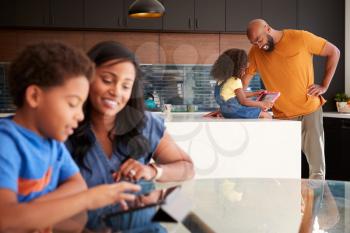 African American Parents Helping Children Studying Homework On Digital Tablets In Kitchen