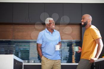 Senior Father Talking And Drinking Coffee With Adult Son In Kitchen At Home