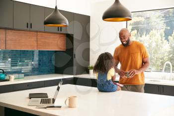 Father With Daughter Sitting On Kitchen Counter At Home Using Digital Tablet