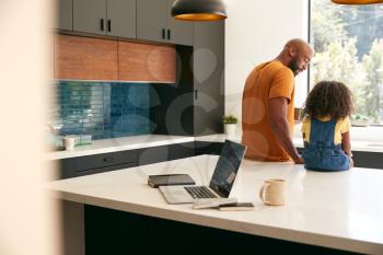 Father With Daughter Sitting On Kitchen Counter At Home Using Digital Tablet