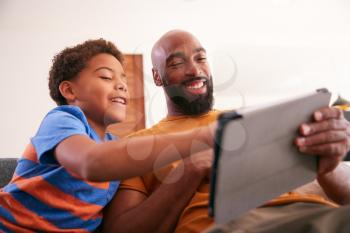 African American Family At Home With Father And Son Sitting On Sofa At Home Using Digital Tablet