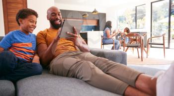 African American Family At Home With Father And Son Sitting On Sofa At Home Using Digital Tablet