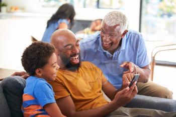 Multi-Generation Male African American Family On Sofa At Home Laughing At Mobile Phone