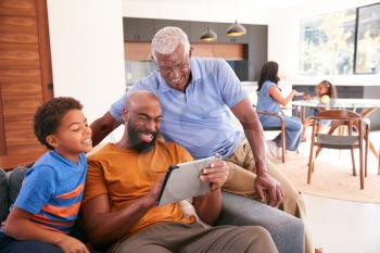 Multi-Generation Male African American Family Sitting On Sofa At Home Using Digital Tablet