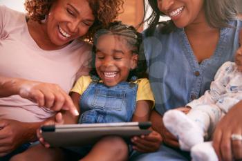 Multi-Generation Female African American Family Sitting On Sofa At Home Using Digital Tablet