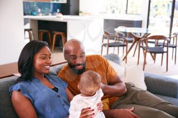 Smiling African American Parents Cuddling And Playing With Baby Daughter Indoors On Sofa At Home
