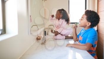 Two Children Brushing Their Teeth In Bathroom At Home